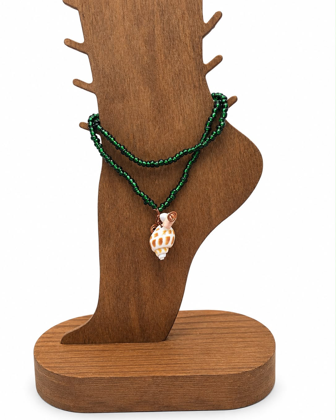 Green beaded bracelet with a shell charm on a wooden stand against a white background