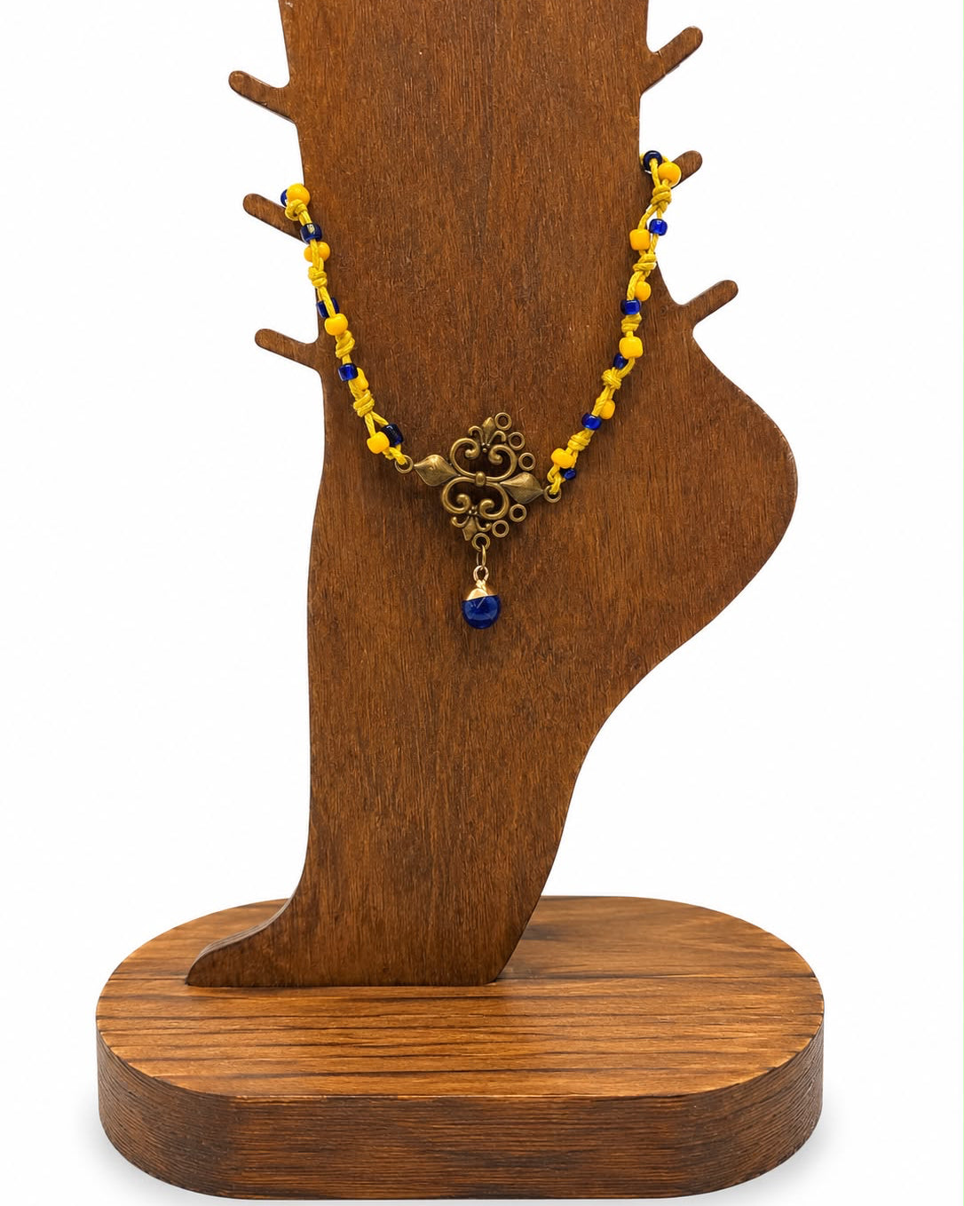 Necklace with yellow beads and a blue pendant on a wooden tree-shaped stand.