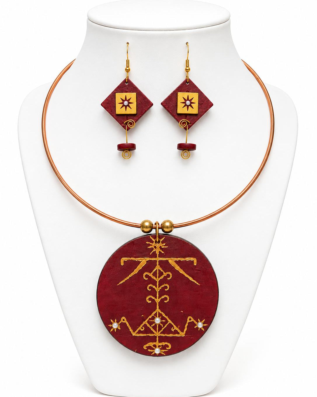 Jewelry set with red and gold circular pendant and matching earrings on a white stand.